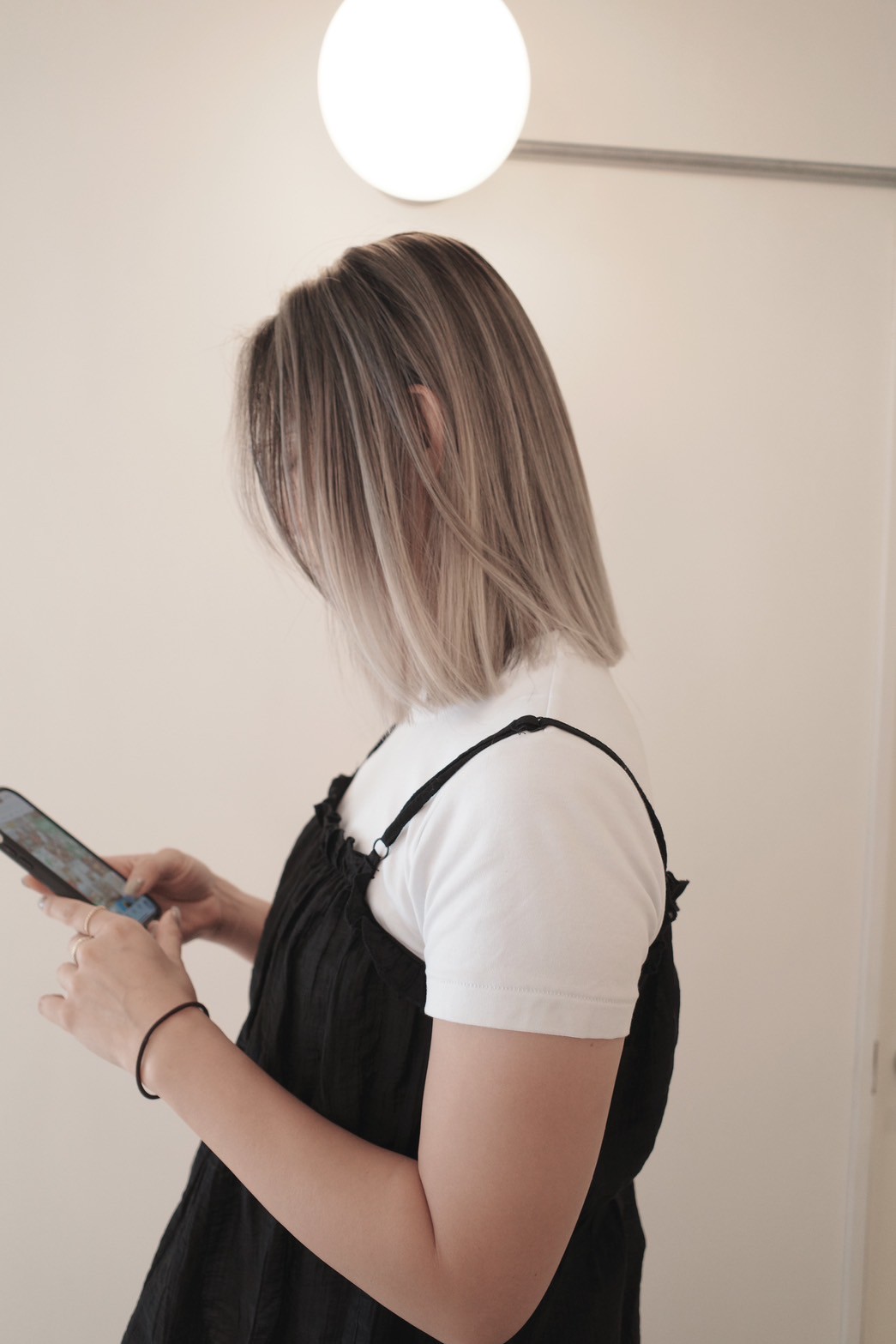 アッシュベージュのグラデーションボブ（横顔、スマートフォン操作中、重ね着スタイル、別角度）