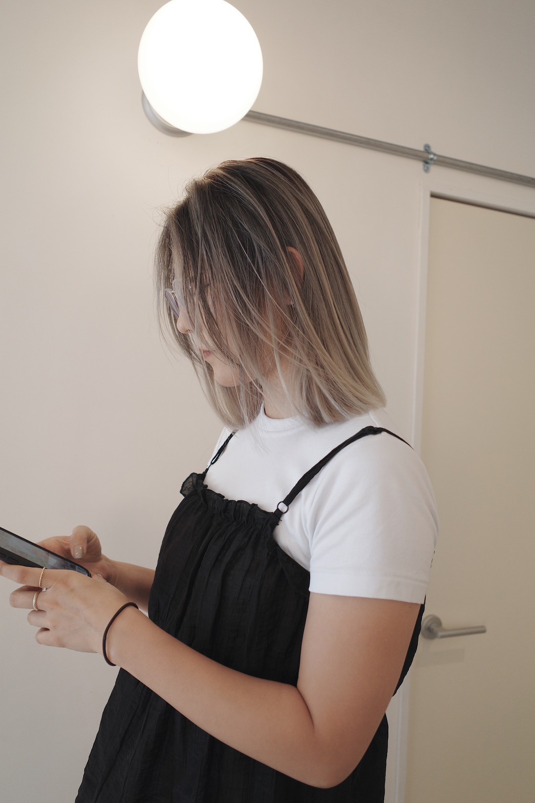 アッシュベージュのグラデーションボブ（横顔、スマートフォン操作中、重ね着スタイル）