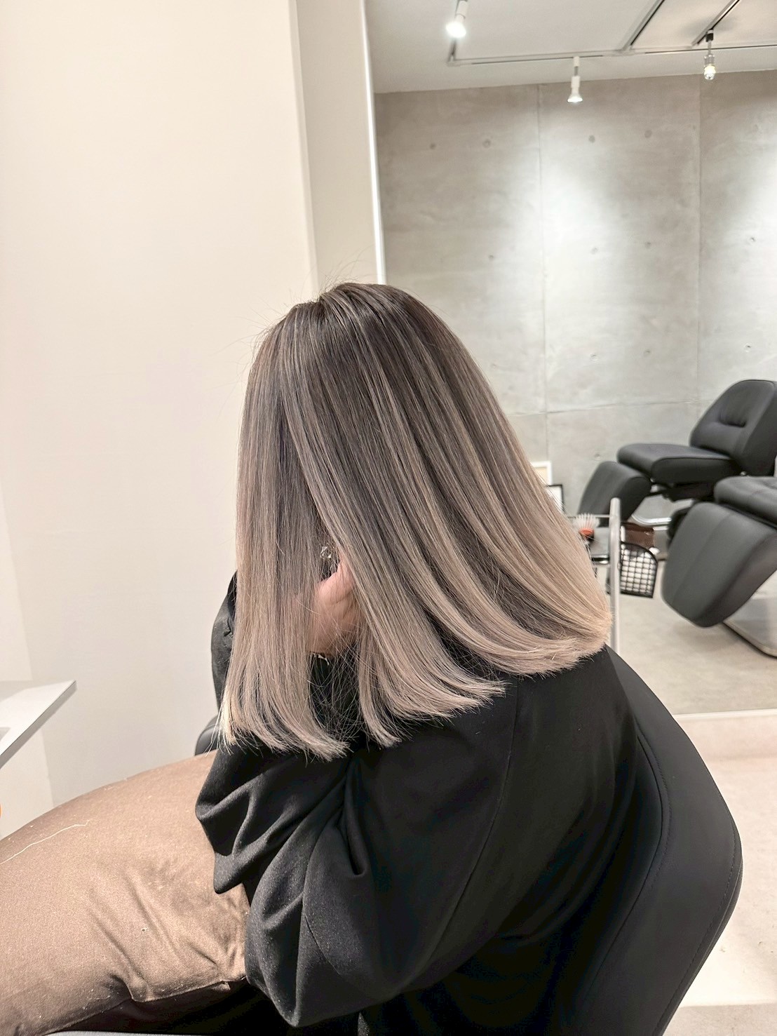 アッシュベージュのミディアムヘアでサロンの椅子に座る女性（横顔）