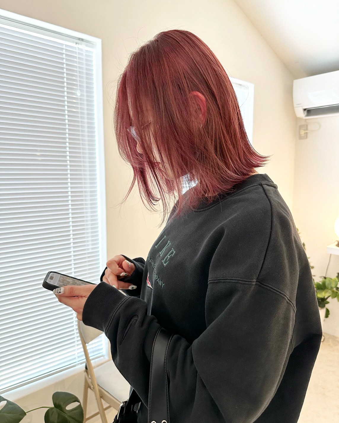鮮やかなレッドのミディアムヘア（横顔、スマートフォン操作中）